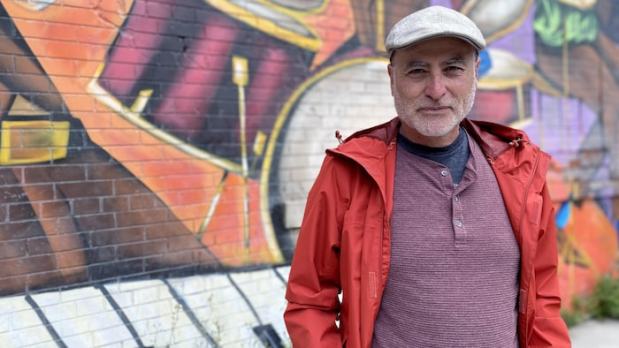 Un homme (Nano Valverde, professeur de musique retraité de la communauté chilienne de Toronto) devant un graffiti dont les éléments visuels évoquent la musique. 